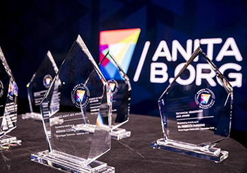 Clear acrylic diamond shaped awards in front of a wall with the AnitaB.org logo